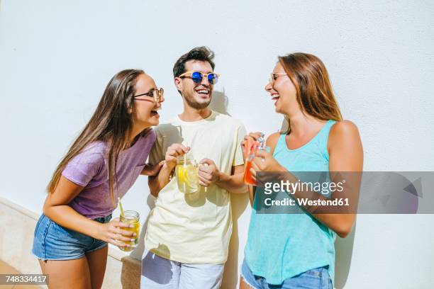 laughing friends holding refreshing drinks in front of white wall - drink stock-fotos und bilder