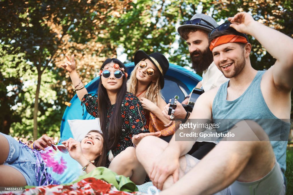 Five young adult friends playing acoustic guitar while festival camping