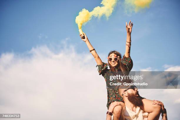 young boho woman holding yellow smoke flare on boyfriends shoulders at festival - festival musicale foto e immagini stock