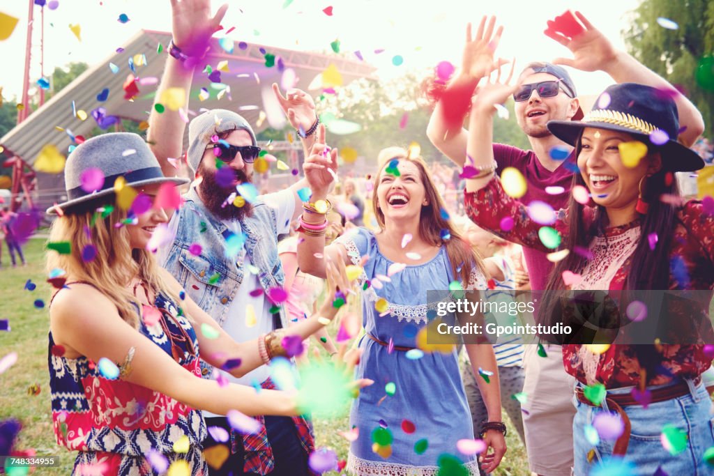 Young adult friends throwing confetti at festival