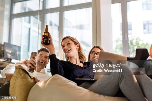 casual business people clinking beer bottles in office - afterwork photos et images de collection