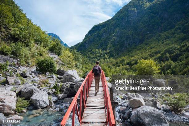 rear view of man crossing bridge, accursed mountains, theth, shkoder, albania, europe - albania stock pictures, royalty-free photos & images