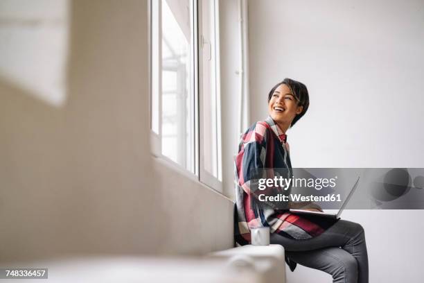 smiling woman sitting at the window using laptop - founders cup portraits fotografías e imágenes de stock