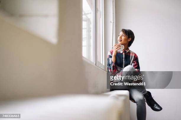 woman sitting at the window holding cup - founders cup portraits fotografías e imágenes de stock