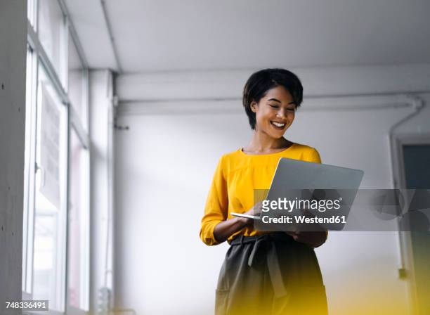 smiling woman using laptop - business woman standing office stock-fotos und bilder