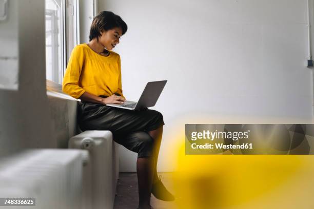 woman sitting at the window using laptop - tech founder stock pictures, royalty-free photos & images