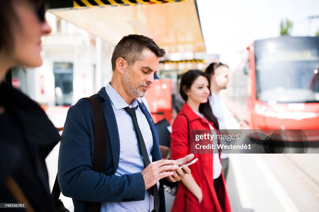 Businessman with smartphone waiting at the bus stop