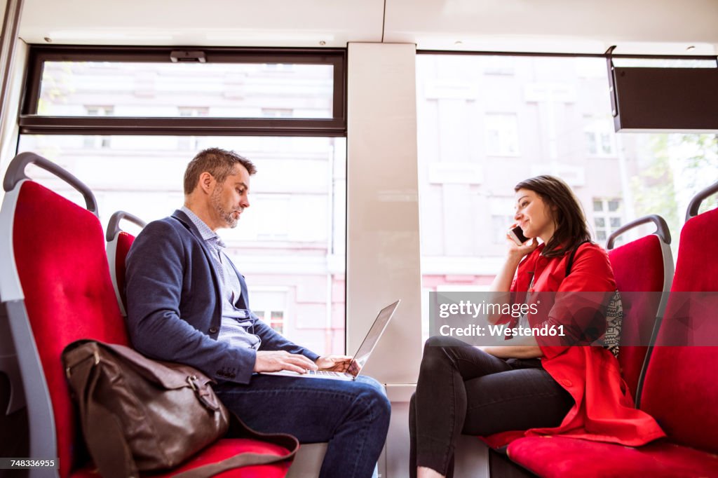 Businessman and woman with laptop and smartphone in bus