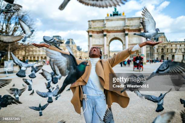 france, paris, happy young woman with flying pidgeons at arc de triomphe - paris stock-fotos und bilder