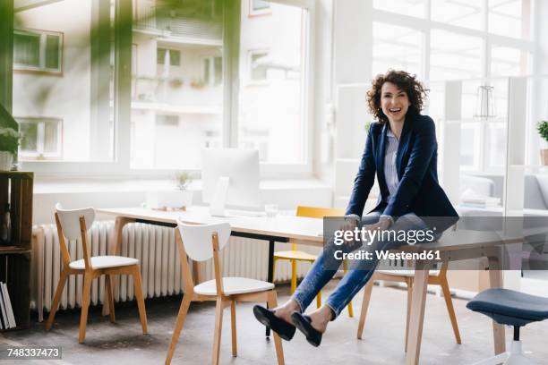 businesswoman in office sitting on desk, having fun - mid volwassen vrouw stockfoto's en -beelden