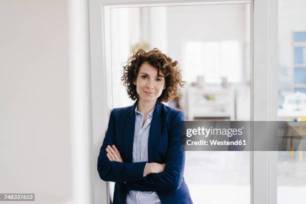 businesswoman standing in her office with arms crossed - business woman standing office stock-fotos und bilder
