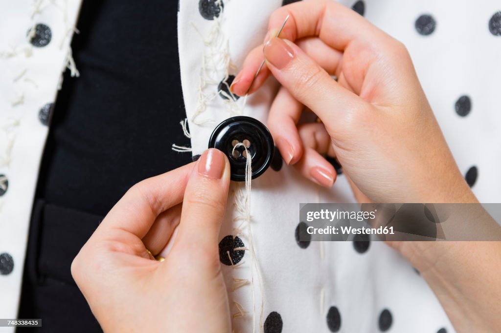 Woman's hands stitching button on a dress, close-up