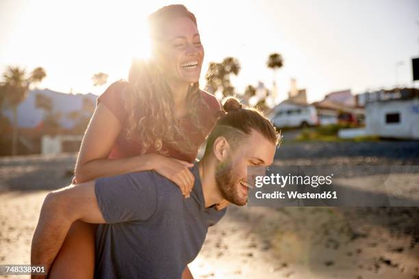 Young man giving his girlfriend a piggyback ride on the beach