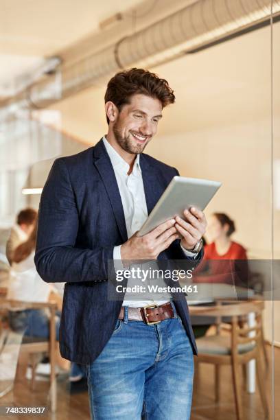 smiling businessman using tablet in office with a meeting in background - boardroom ipad stock-fotos und bilder