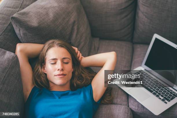 young woman with laptop lying on couch at home - resting stock-fotos und bilder