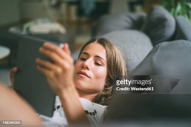 relaxed young woman lying on couch using tablet - e reader stock pictures, royalty-free photos & images