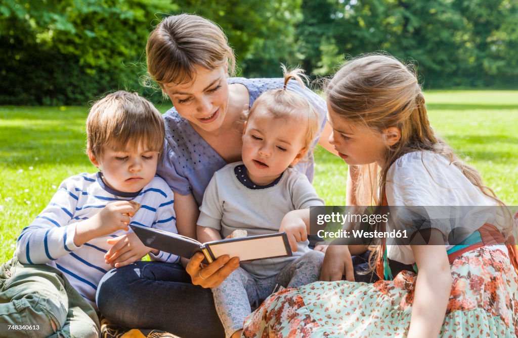 Mother showing photo album to children on meadow