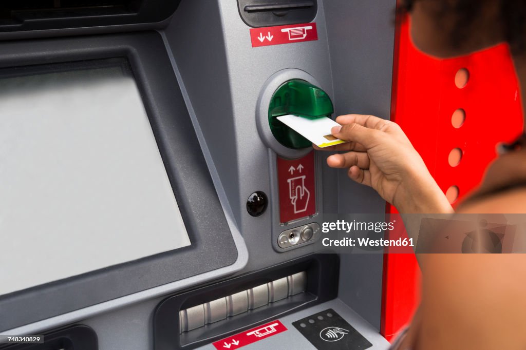 Woman pushing credit card at cash dispenser, partial view