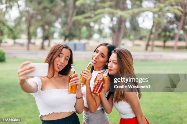 playful friends in a park drinking beer and taking a selfie - beer bottle mouth stock-fotos und bilder