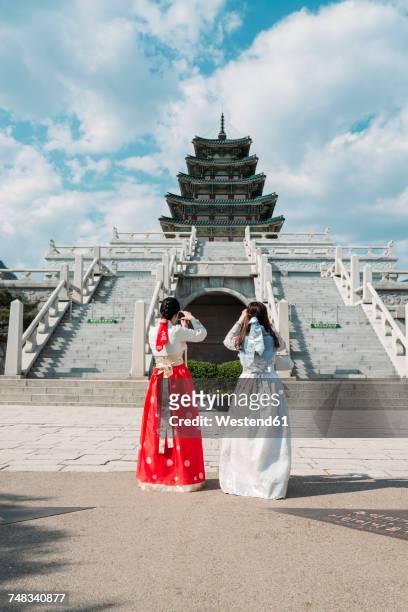 south korea, seoul, tow women wearing traditional korean dresses taking photos of the national folk museum of korea, inside gyeongbokgung palace - korea palace stock pictures, royalty-free photos & images