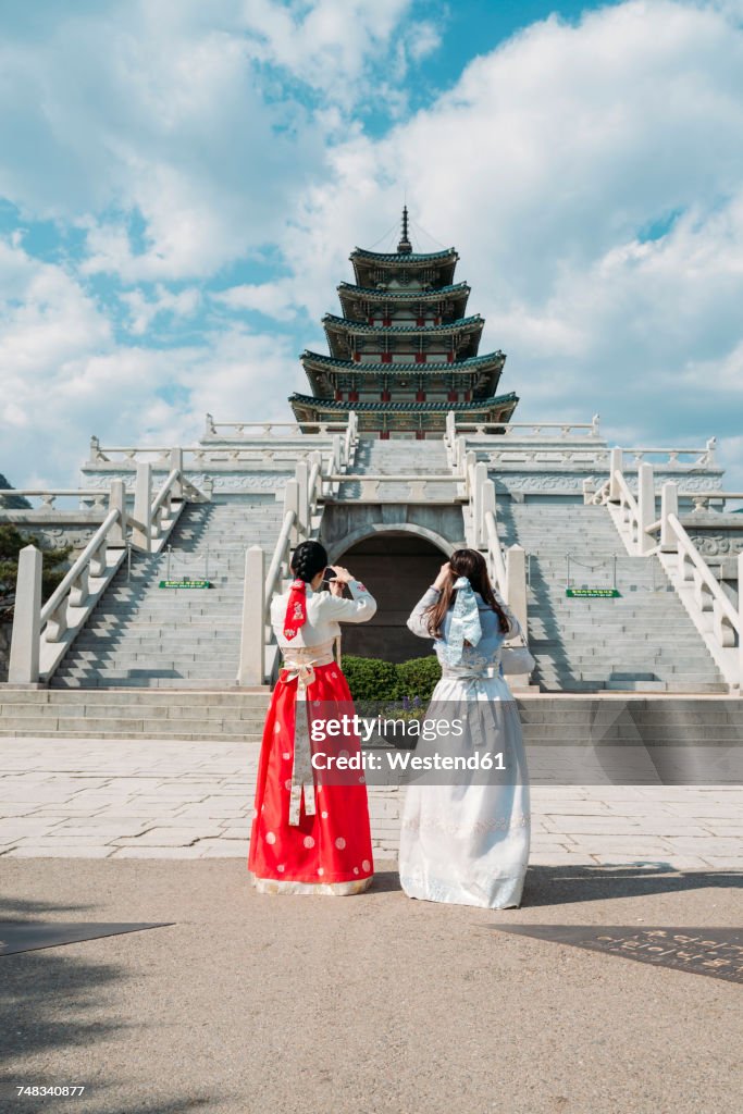 South Korea, Seoul, tow women wearing traditional Korean dresses taking photos of the National Folk Museum of Korea, inside Gyeongbokgung Palace