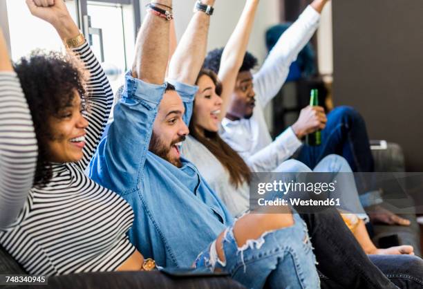 excited friends sitting on the sofa raising their arms - beer bottle mouth stock-fotos und bilder