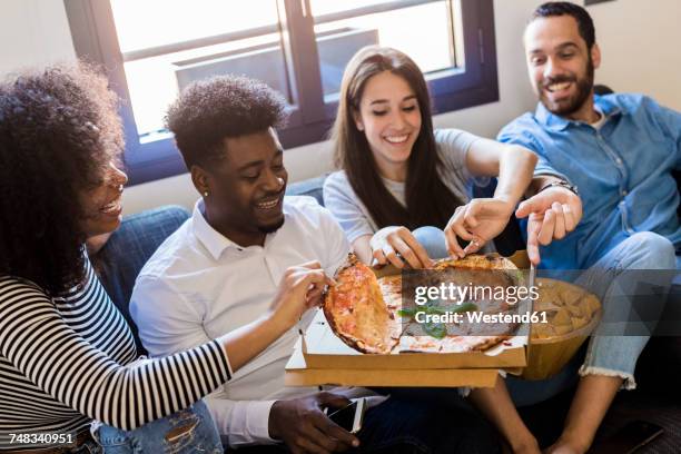 happy friends sitting on the sofa sharing a pizza - pizza box stock-fotos und bilder