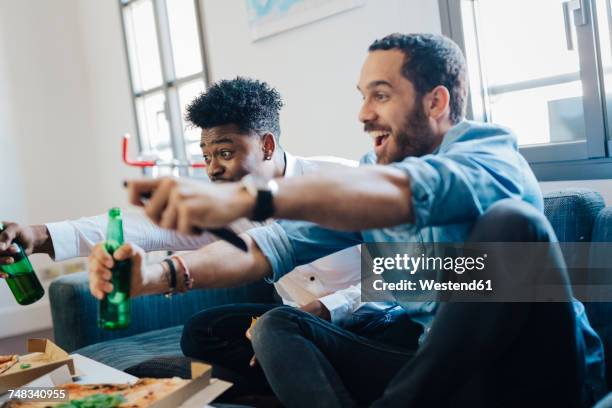 excited friends with beer bottles sitting on the sofa cheering - beer bottle mouth stock-fotos und bilder
