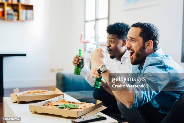 excited friends with beer bottles sitting on the sofa cheering - beer bottle mouth stock-fotos und bilder