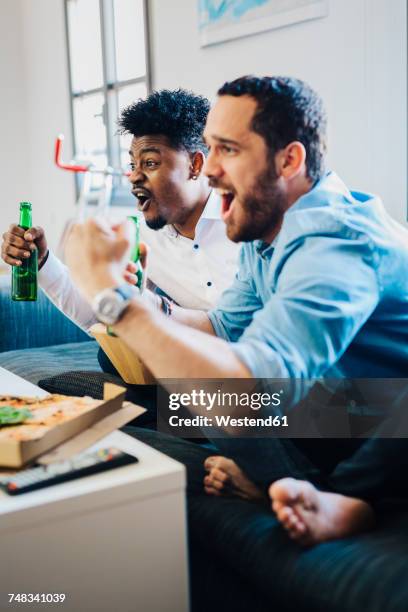 excited friends with beer bottles sitting on the sofa cheering - beer bottle mouth stock-fotos und bilder