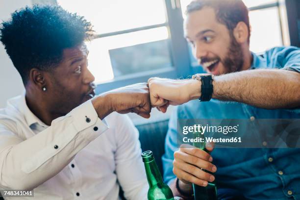 excited friends with beer bottles sitting on the sofa bumping fists - champions day two stockfoto's en -beelden