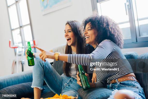 excited friends with beer bottles sitting on the sofa watching tv - beer bottle mouth stock-fotos und bilder