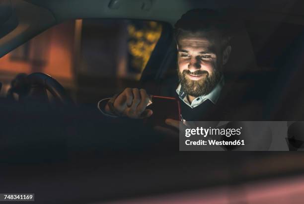 smiling businessman using cell phone in car at night - light car night stock-fotos und bilder