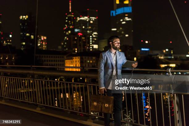 young man with tablet and earphone on urban bridge at night - man business hipster dark smile stock pictures, royalty-free photos & images
