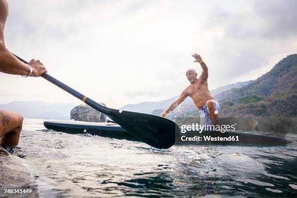 mexico, banderas bay, los arcos national marine park, man falling from paddleboard - mature paddleboard stock pictures, royalty-free photos & images