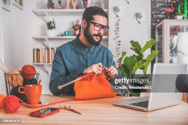 bearded man knitting at home using laptop for watching online tutorial - entsättigt stock-fotos und bilder