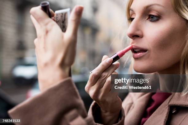 businesswoman applying lipstick outdoors - beautiful woman lipstick stock-fotos und bilder