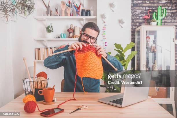 bearded man knitting at home using laptop for watching online tutorial - masche stock-fotos und bilder