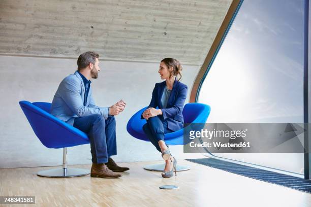 man and woman sitting on chairs talking - abbigliamento elegante foto e immagini stock