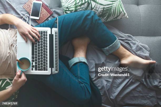 Man using laptop and drinking coffee on sofa bed, partial view