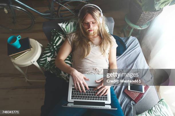 man with long hair and beard using laptop on sofa bed - faulheit stock-fotos und bilder