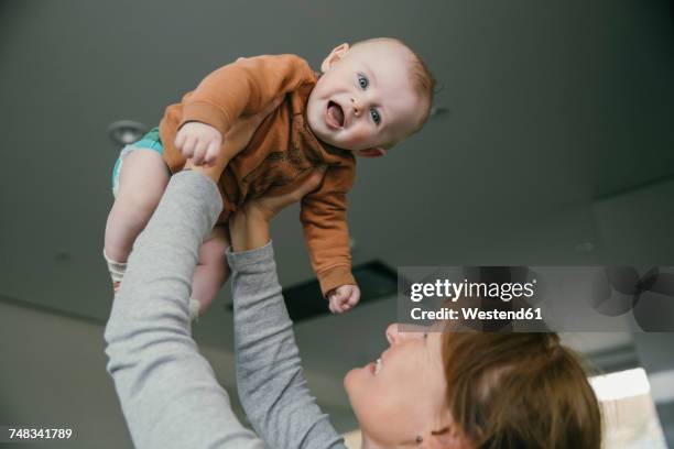 grandmother lifting up baby at home - raising baby stock-fotos und bilder
