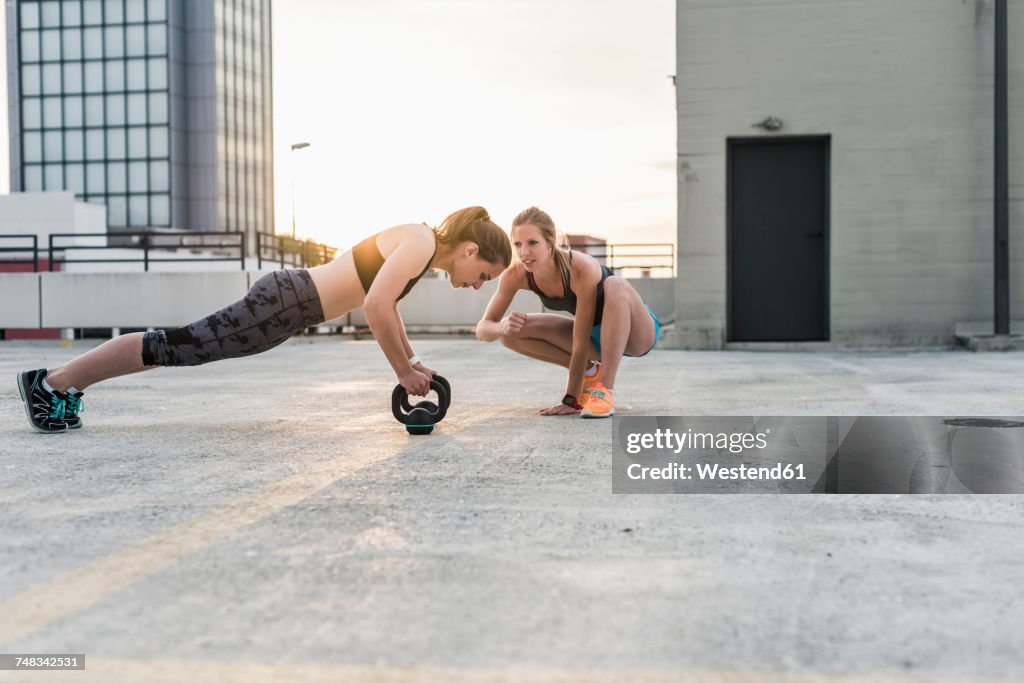 Woman cheering at training partner kettlebell on parking level in the city