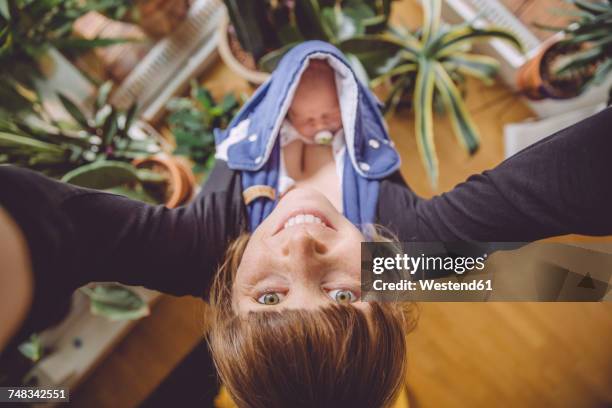 mother taking a selfie at home with newborn baby in carrier - baby eltern von oben stock-fotos und bilder