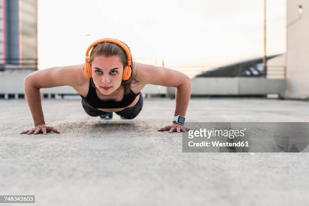 woman with headphones doing pushups on parking level in the city - push ups stock-fotos und bilder