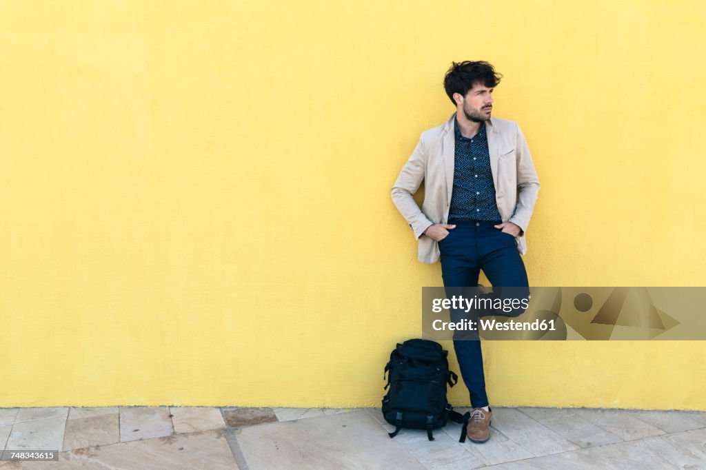 Young man with backpack standing in front of yellow wall