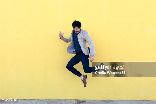 young man jumping in the air in front of yellow wall - saltare foto e immagini stock