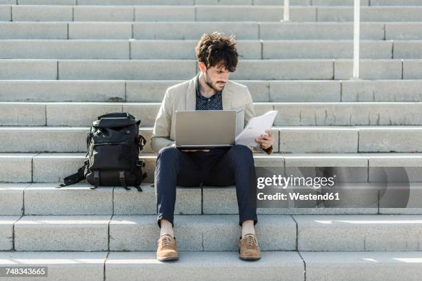 pensive man with laptop sitting on steps checking documents - business studies stockfoto's en -beelden