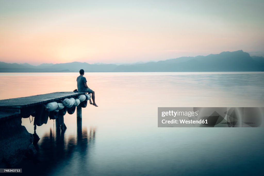 Italy, Lazise, man sitting on jetty looking at Lake Garda