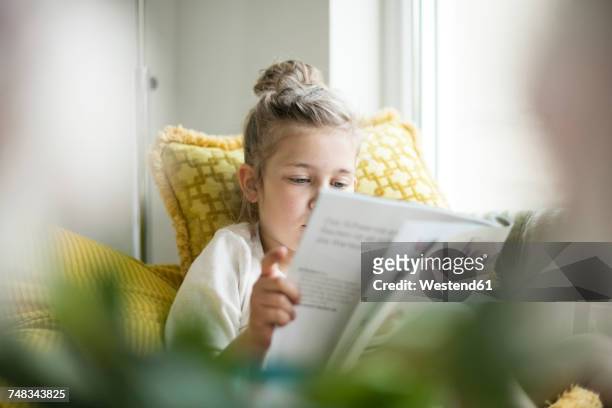 portrait of relaxed little girl sitting on armchair reading magazine - reading stock-fotos und bilder